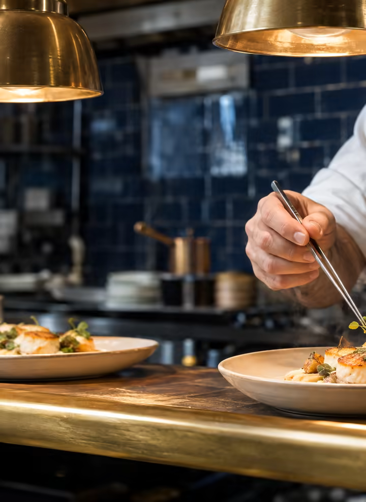 A chef's hands plating seared scallops at the pass.